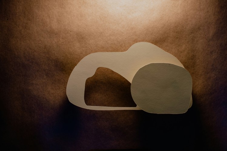 Paper cutout illustration of an empty tomb with the stone rolled away against a textured background.