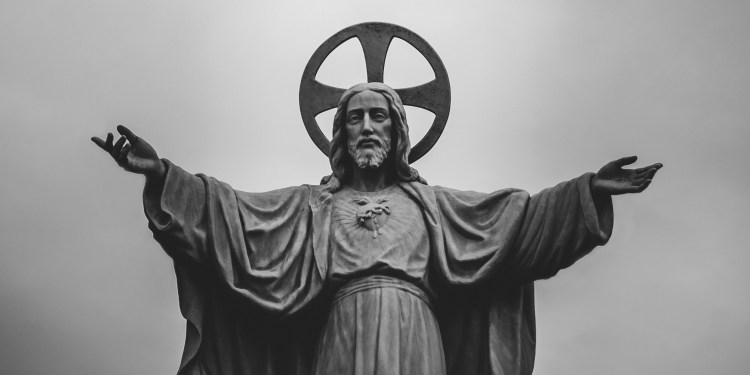 Statue of Jesus with arms outstretched and a halo against a gray sky.